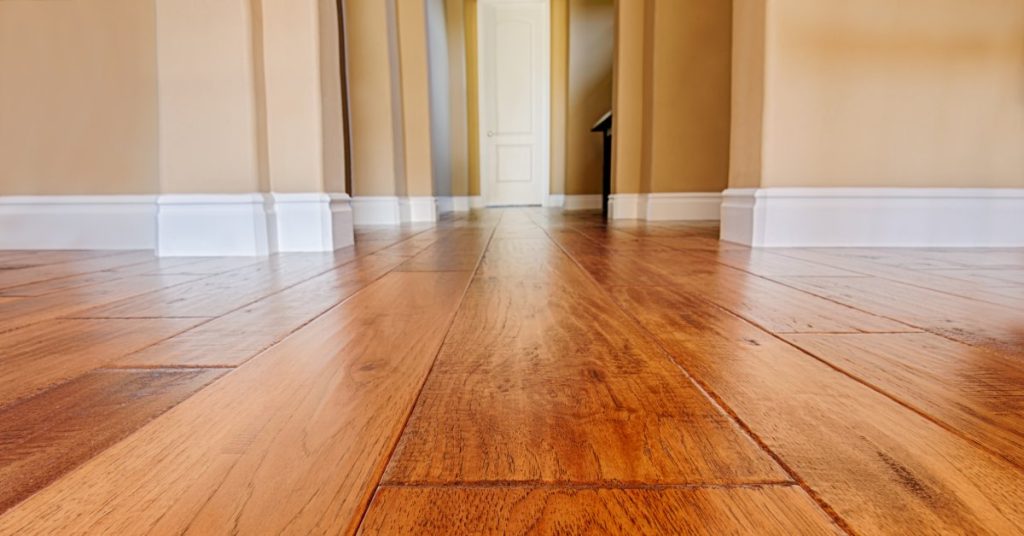Closeup of warm, medium-toned hardwood floors with tan-painted walls and a white door in the background.