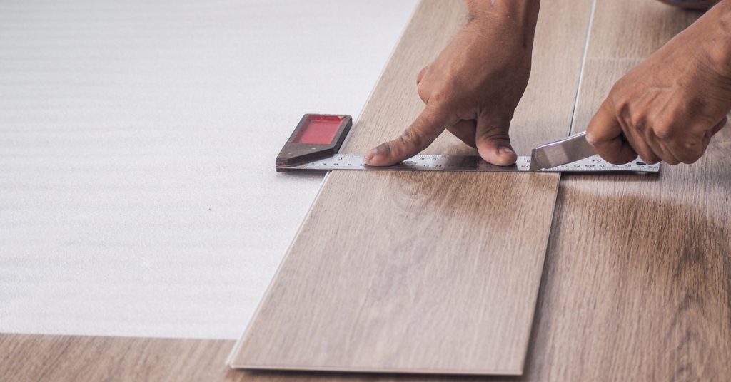 Close-up of a man’s hands using a ruler and a cutter to trim luxury vinyl floor planks before installing them.