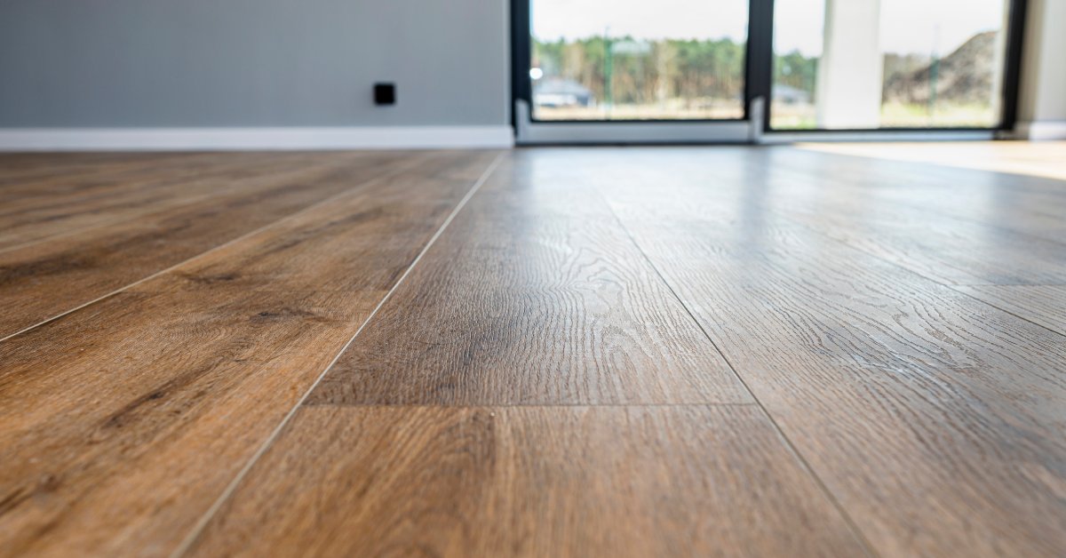 A close-up of light brown vinyl wood flooring in the foreground and a grey wall and two sliding glass doors in the background.