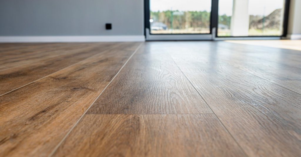 Vinyl flooring in front of sliding doors inside a home with gray walls. The sliding doors look outward to a yard.