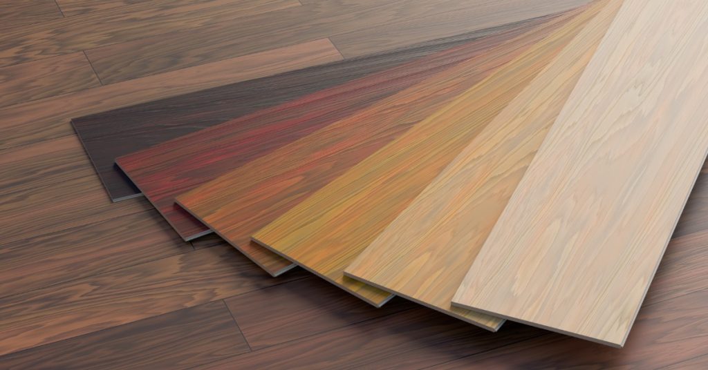 Six planks of hardwood flooring stacked on top of a wooden floor. The hardwood planks are all different colors.